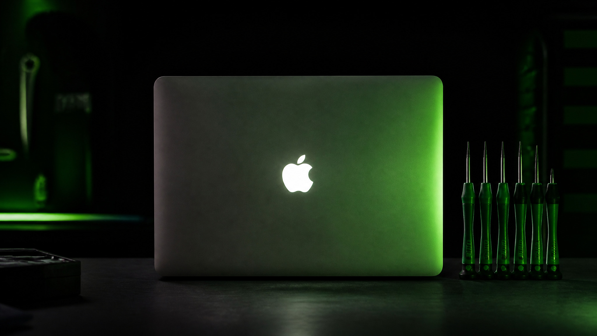 MacBook Pro closed on dark bench with Apple logo prominent and green Wiha precision screwdriver set