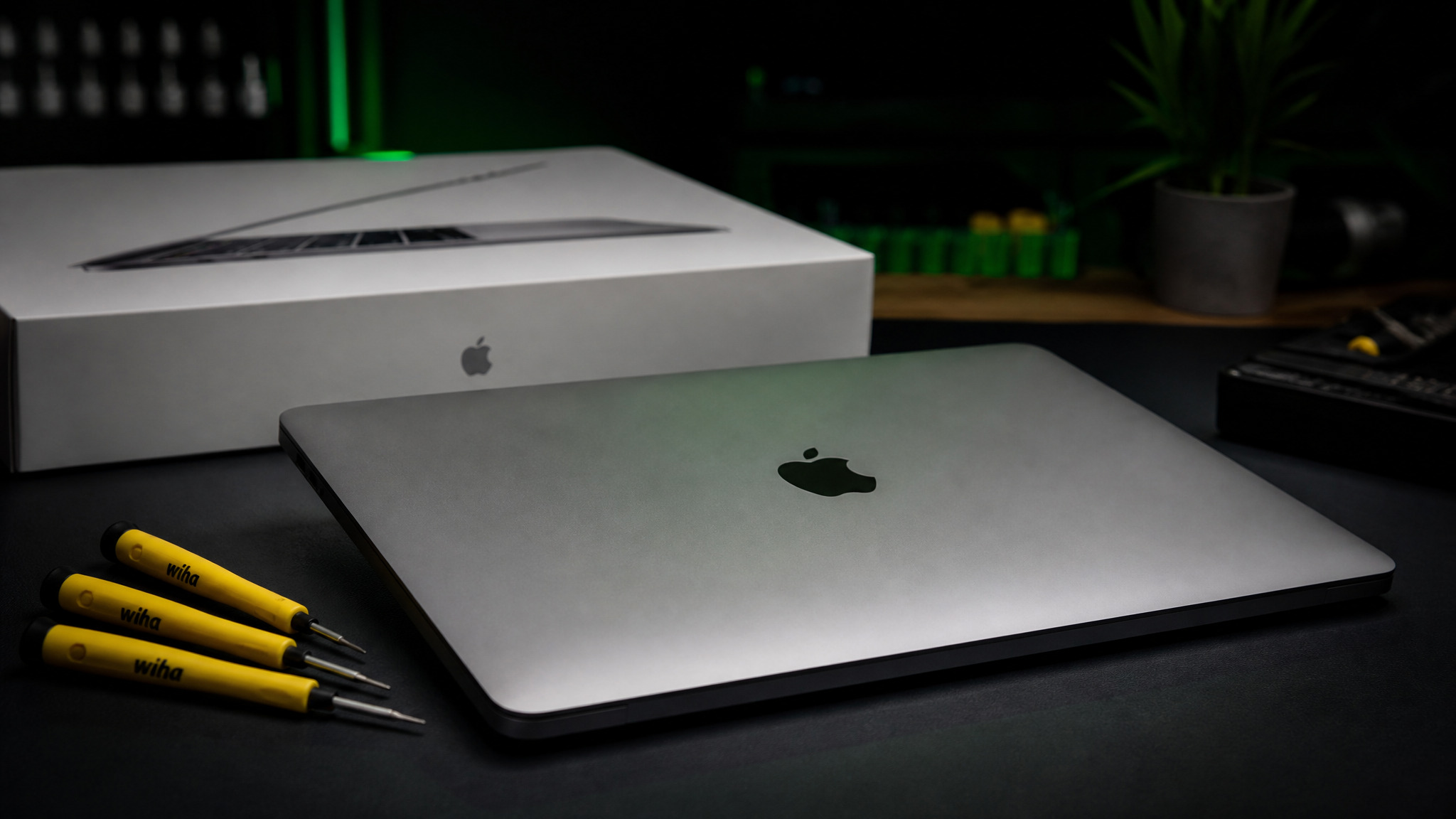 MacBook Pro on dark bench with Apple retail box behind and yellow Wiha tools