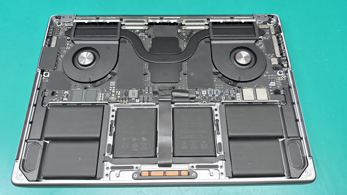 Inside a MacBook Pro showing the dual-fan cooling system, battery cells, and Apple Silicon logic board