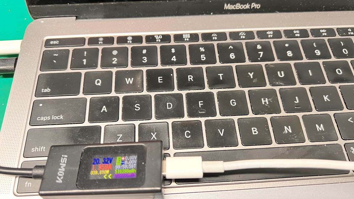 MacBook Pro USB-C port with a power meter showing voltage and amperage during charging diagnostics