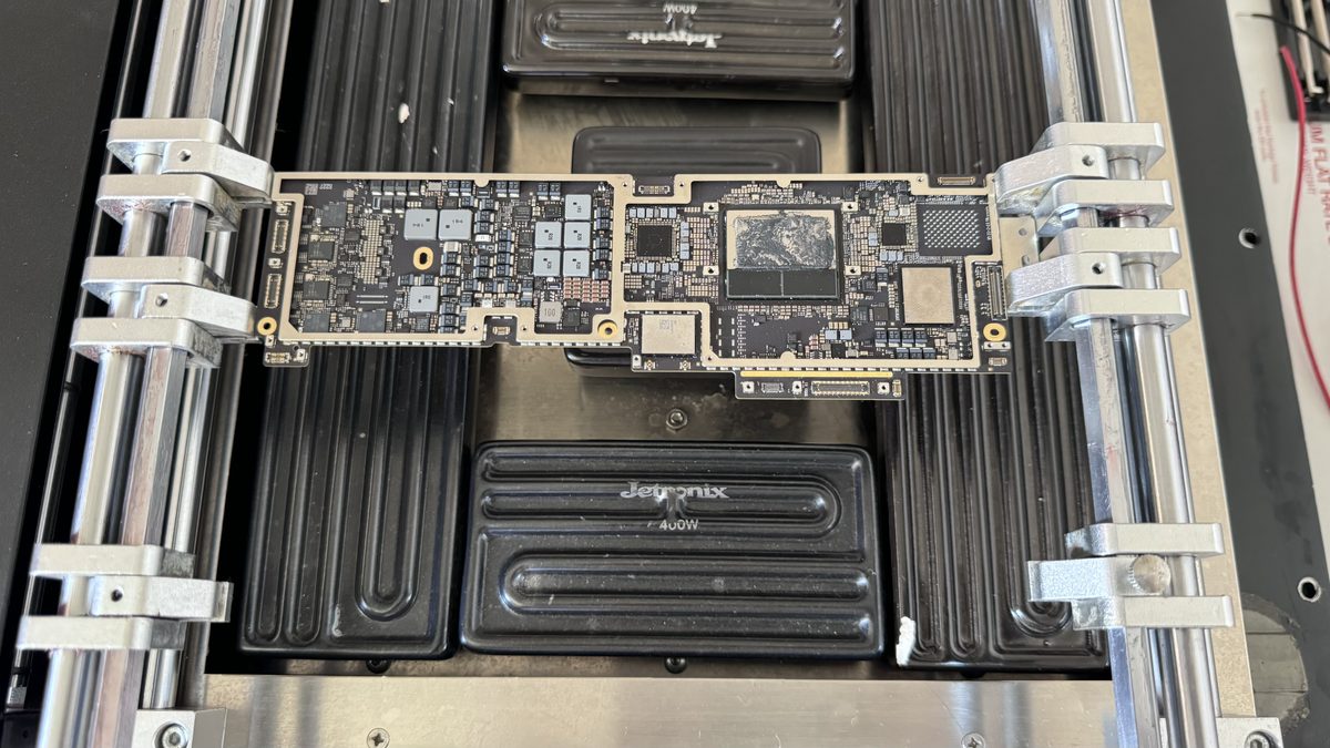 A cleaned MacBook logic board being inspected under a microscope after ultrasonic treatment