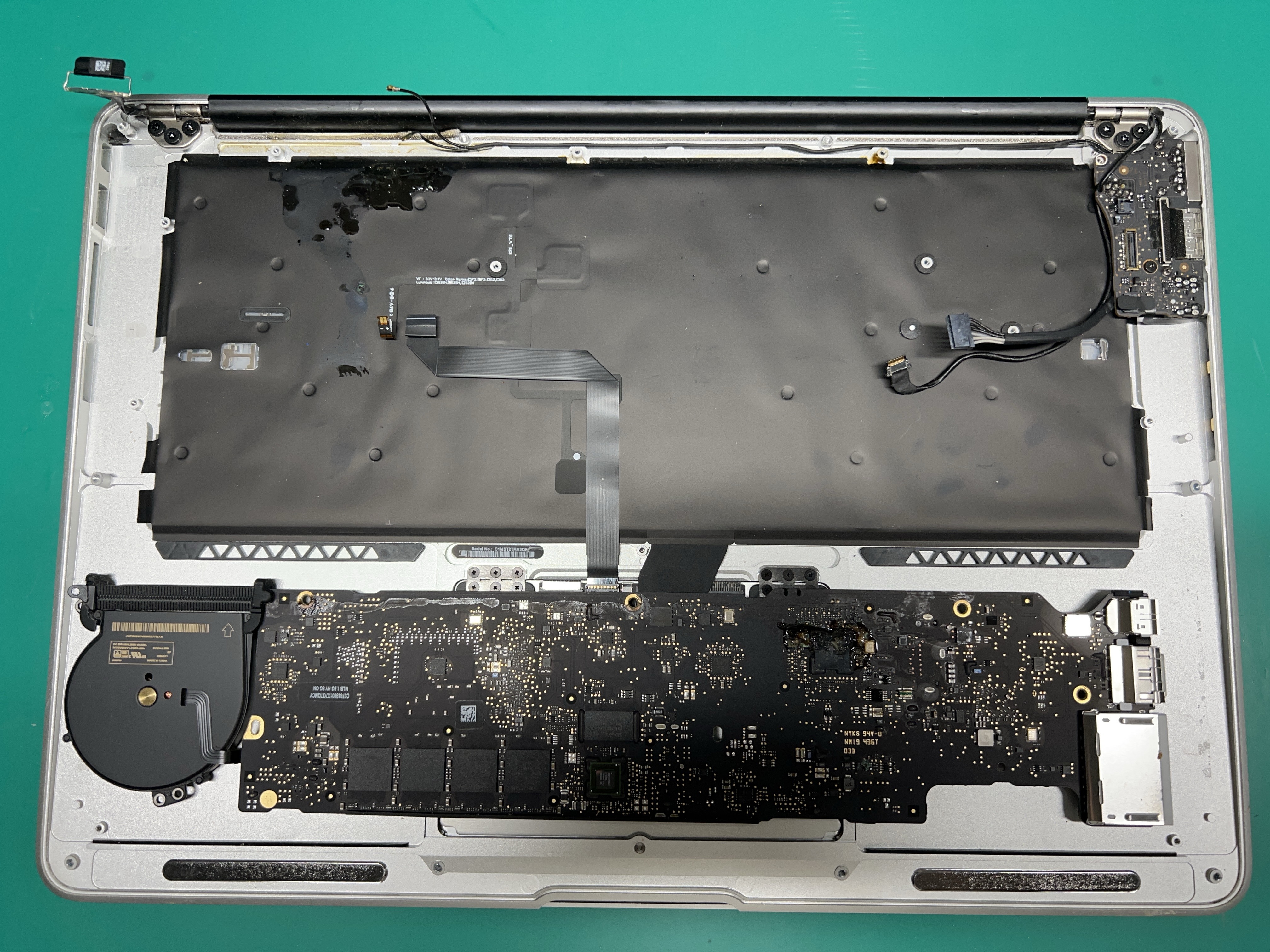 Close-up of a MacBook logic board showing corrosion and damaged components from liquid exposure