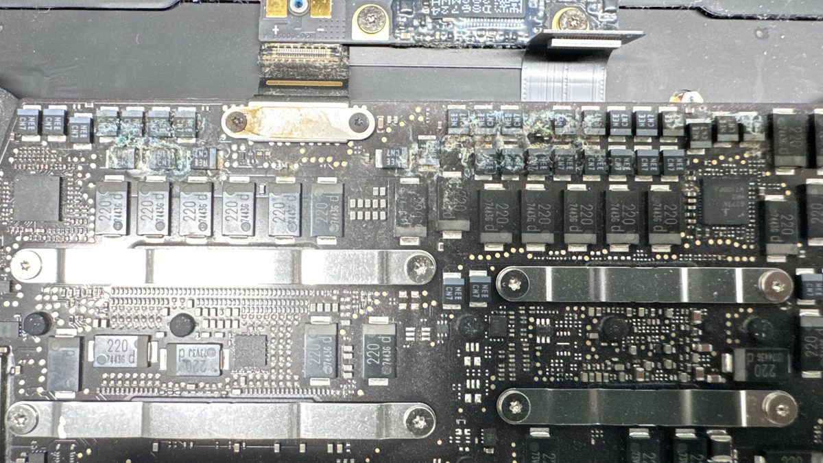 Close-up of corrosion spreading across the copper traces and components of a water-damaged MacBook logic board