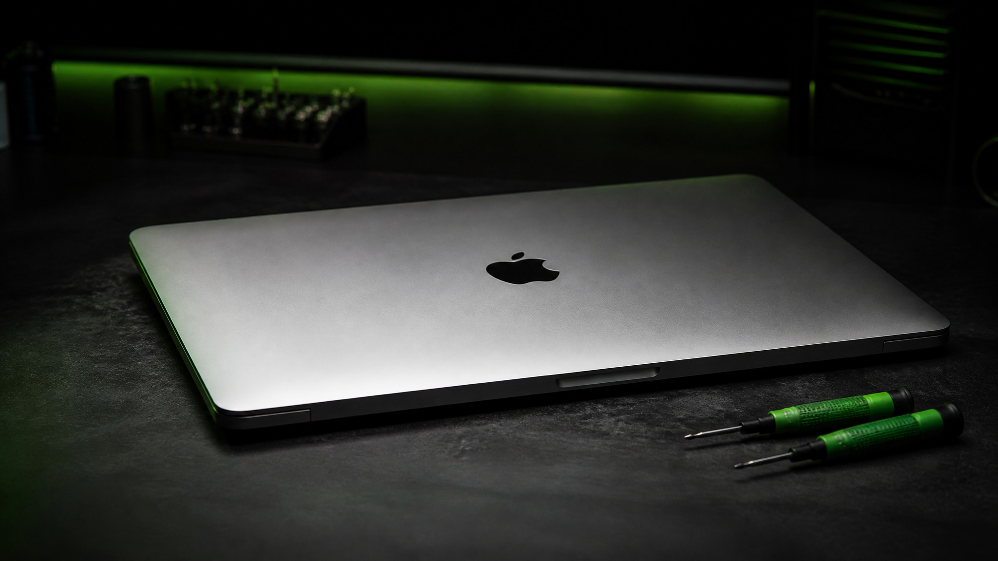 MacBook Pro 15-inch closed on dark repair bench with Apple logo on lid and green Wiha precision screwdrivers