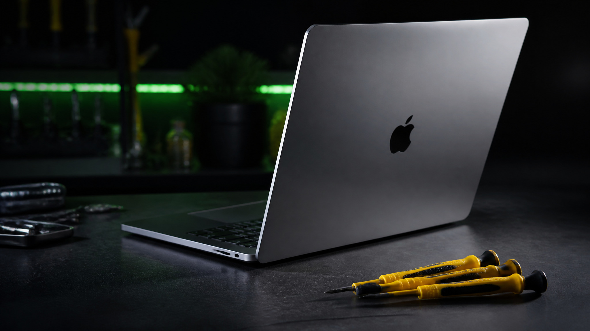 MacBook Pro open at angle showing grey screen with Apple logo visible and yellow Wiha precision tools
