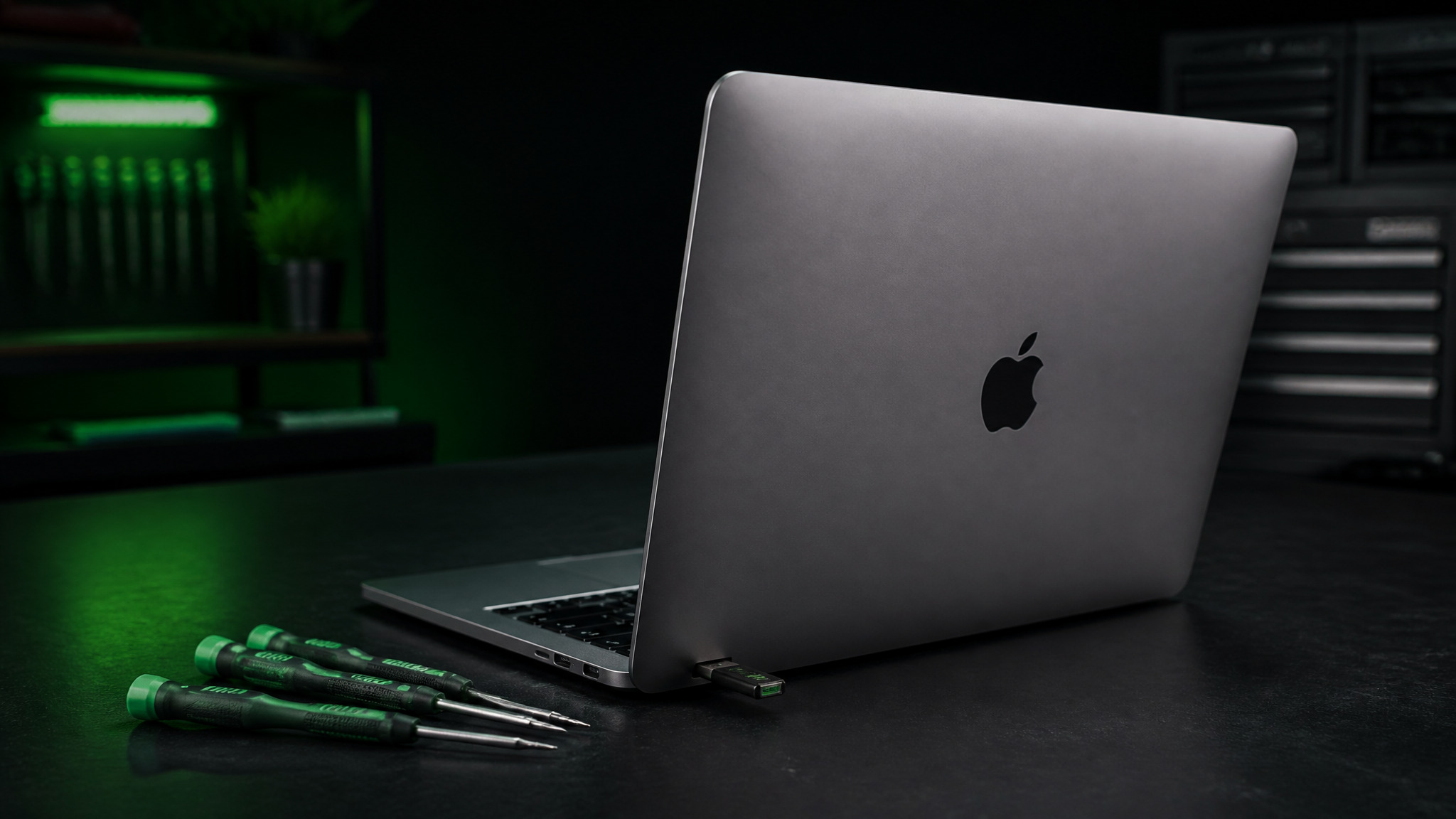 MacBook Pro open with USB flash drive in side port and green Wiha screwdrivers on dark bench