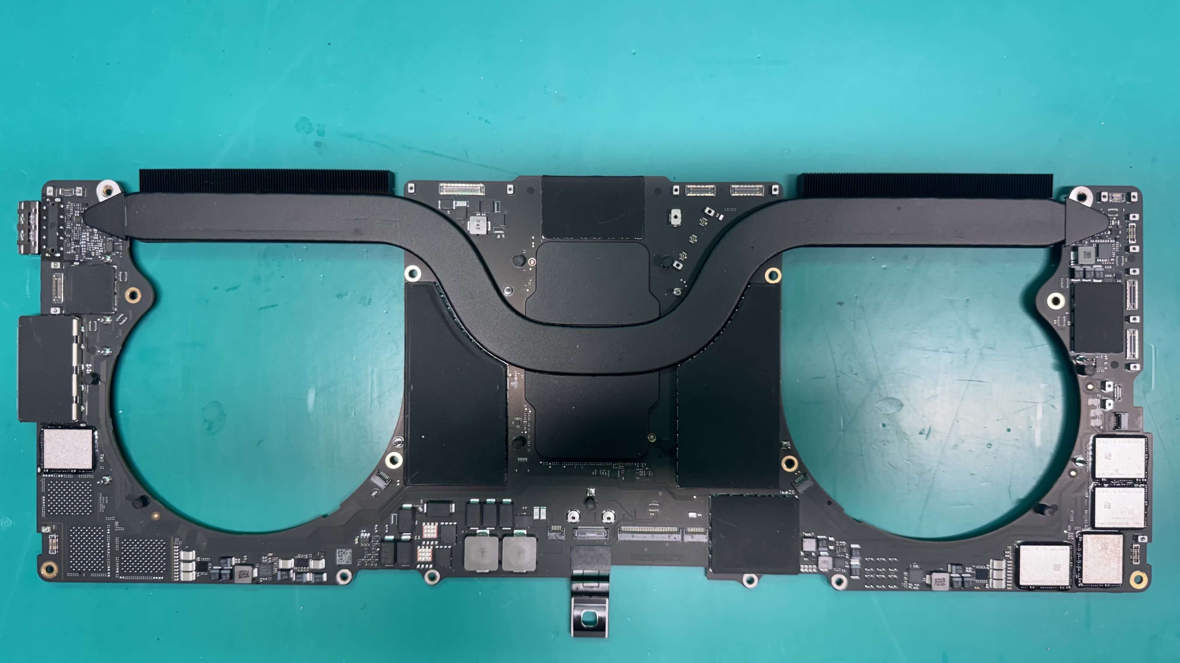 MacBook logic board removed and laid flat on a repair workbench