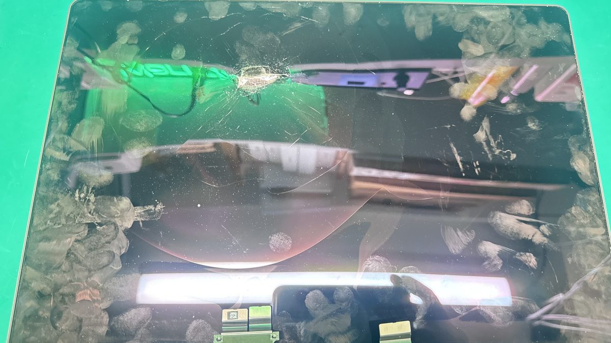 A cracked MacBook Pro Retina display panel with visible impact point and spider-web fractures across the glass