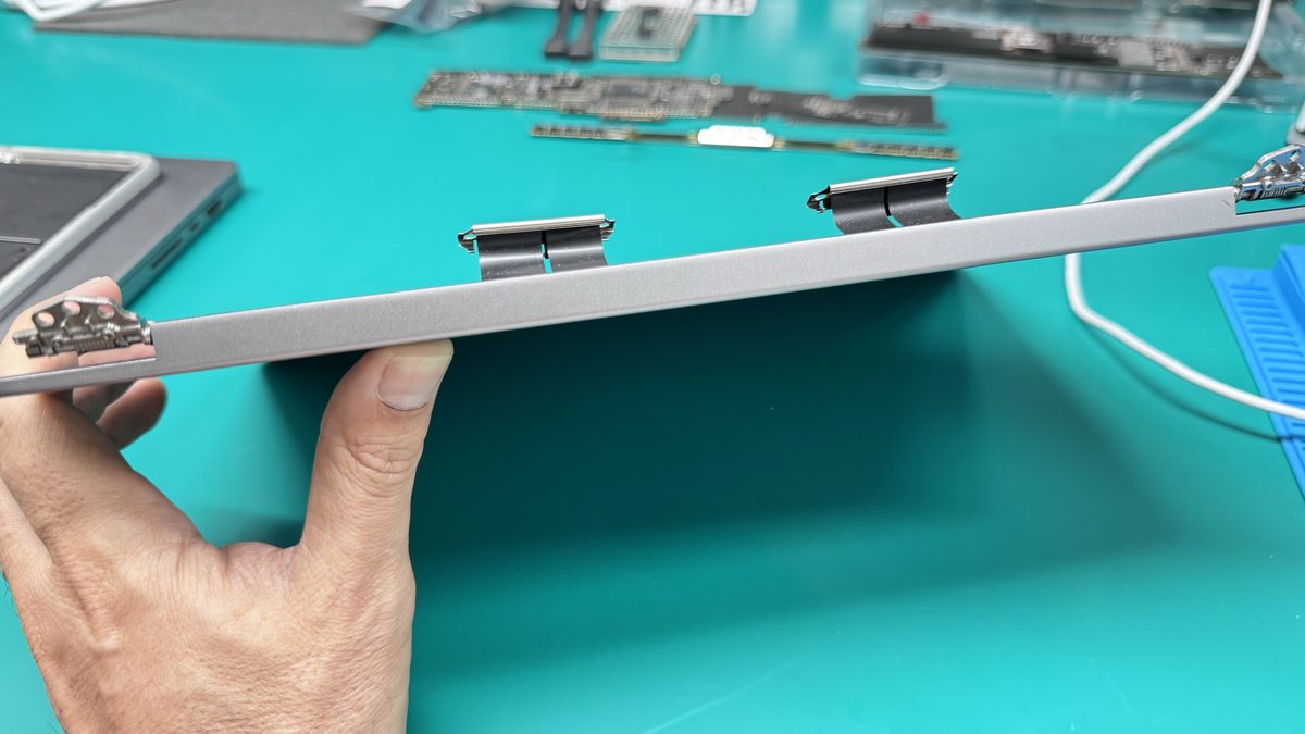 Technician holding a MacBook Pro display assembly showing the hinges during a Retina panel replacement