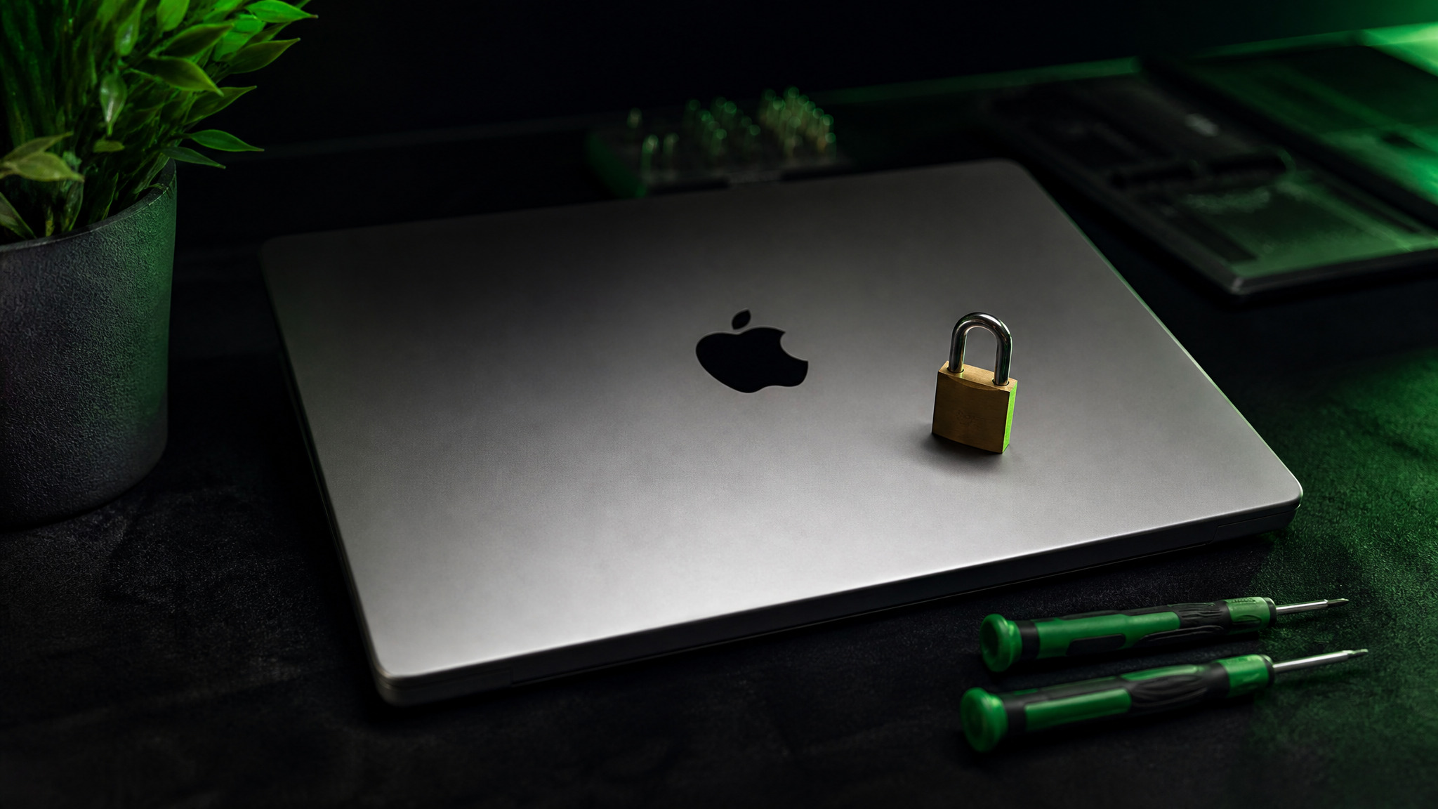 MacBook Pro closed with Apple logo and brass padlock on lid beside green Wiha precision screwdrivers