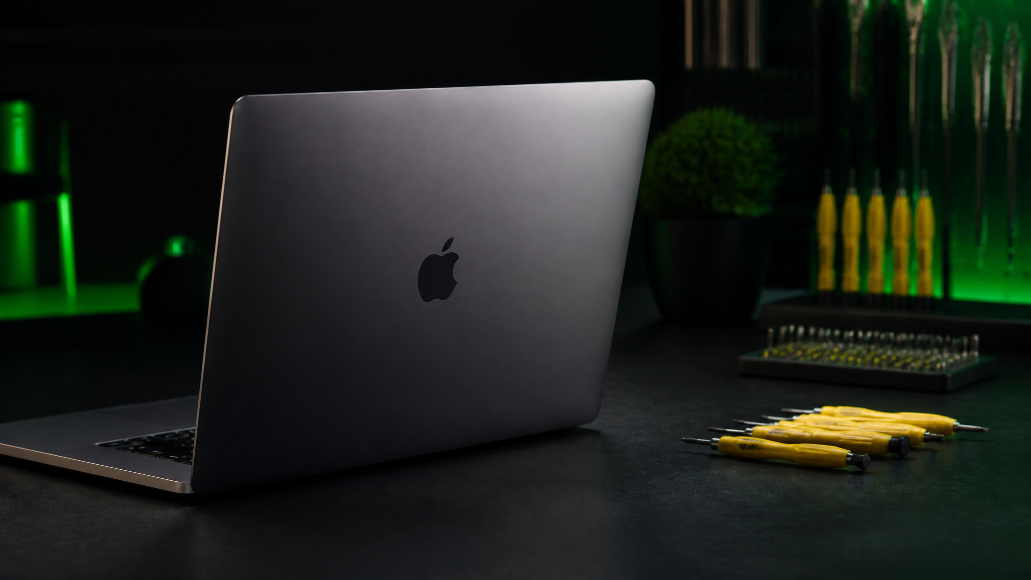 MacBook Pro open showing dark blank screen on repair bench with yellow Wiha precision tools