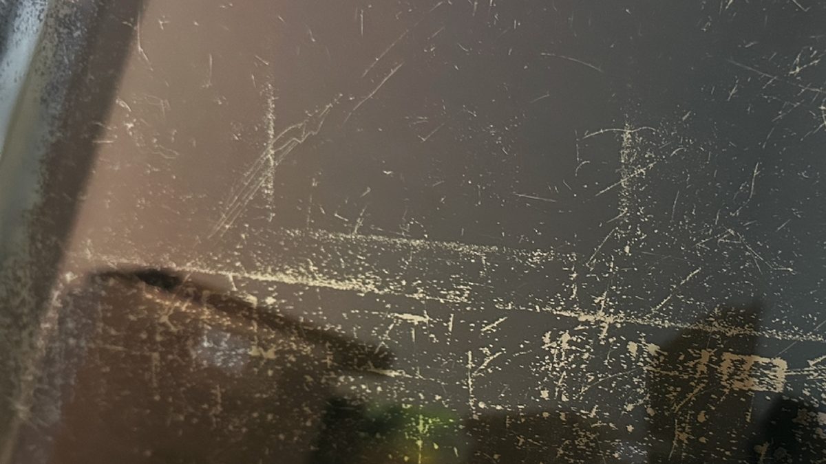 Close-up of delaminated anti-reflective coating on a MacBook Retina display showing scratches and worn patches on a dark screen