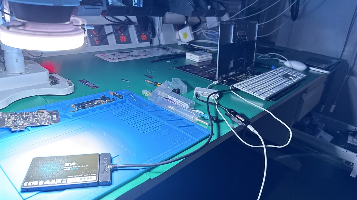 WarriorMac data recovery bench with a MacBook logic board under a microscope and an external SSD connected