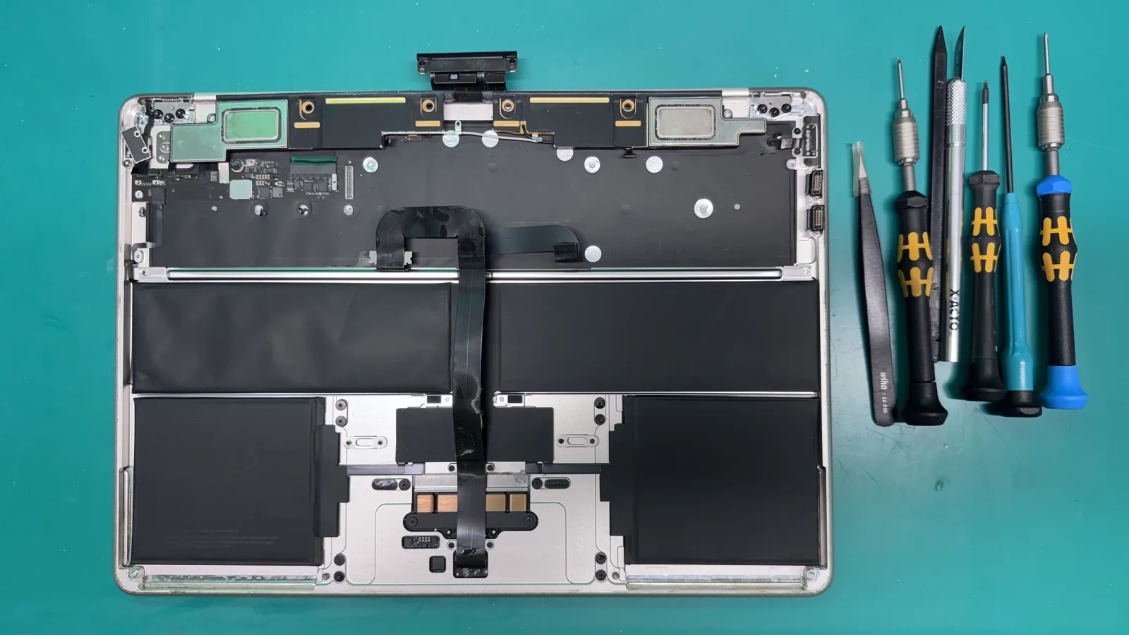 Inside of a MacBook Air showing the top case, battery cells, and keyboard ribbon cable during a liquid damage inspection at WarriorMac in Tampa