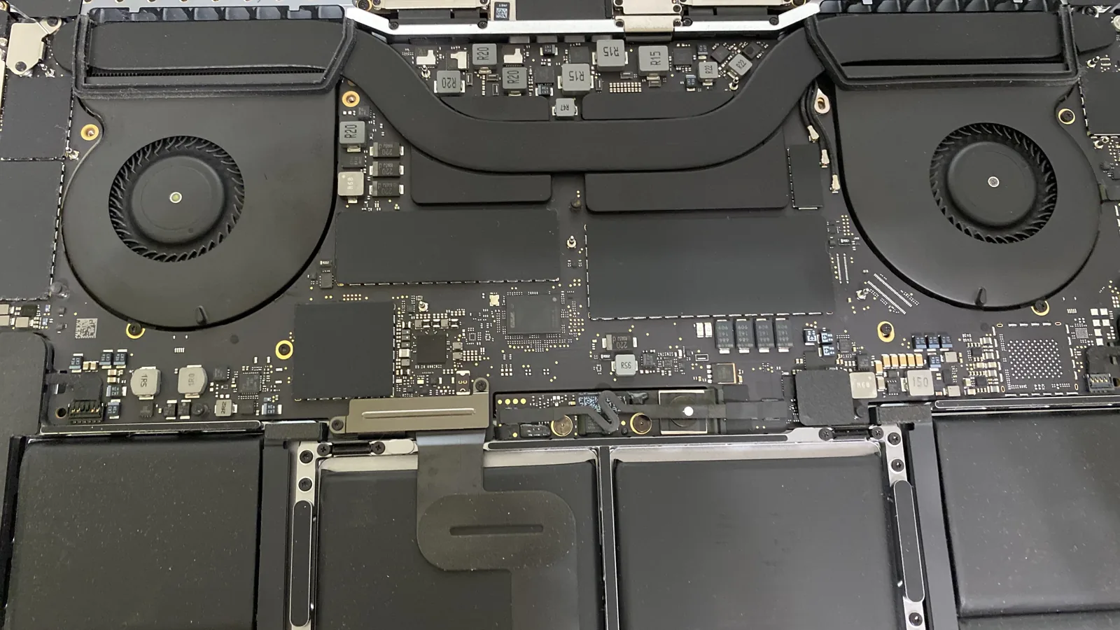 Inside of a MacBook Pro showing the logic board, cooling fans, heat pipes, and battery cells during a repair at WarriorMac in Tampa