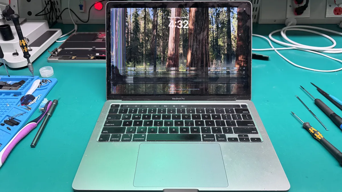 MacBook Pro with a damaged display showing distorted lines, on the repair bench at WarriorMac