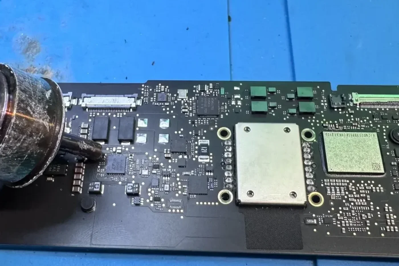 Apple Certified technician performing component-level micro-soldering on a Mac logic board under a microscope