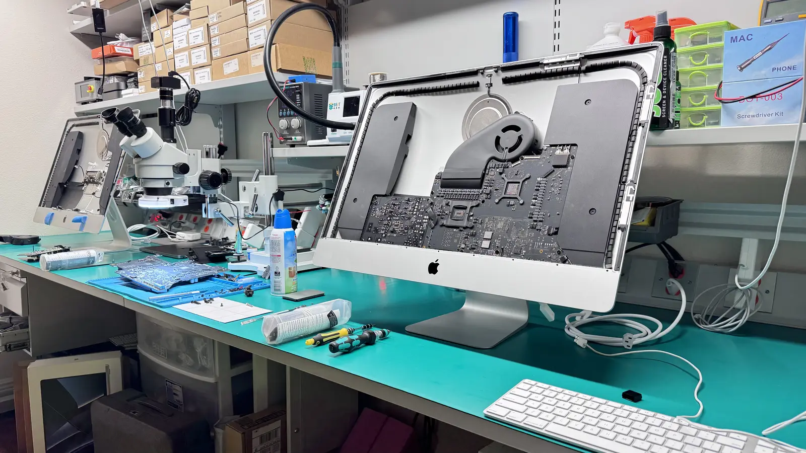 iMac opened on WarriorMac repair workbench showing logic board, microscope, and repair tools in Tampa