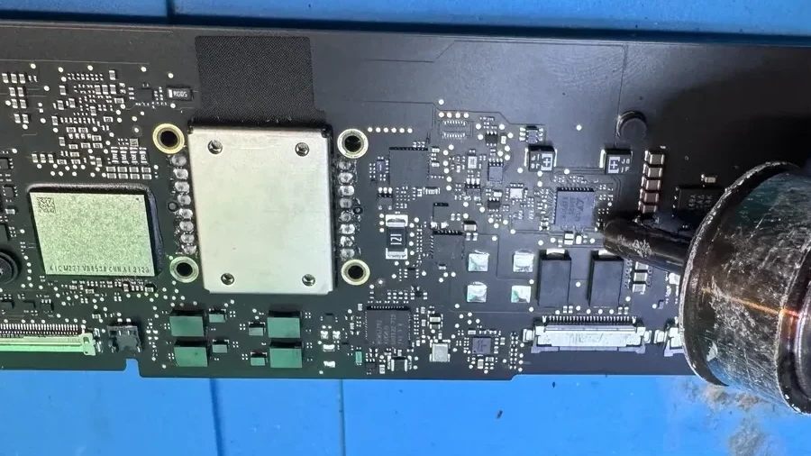 Apple Certified technician performing component-level micro-soldering on a Mac logic board under a microscope