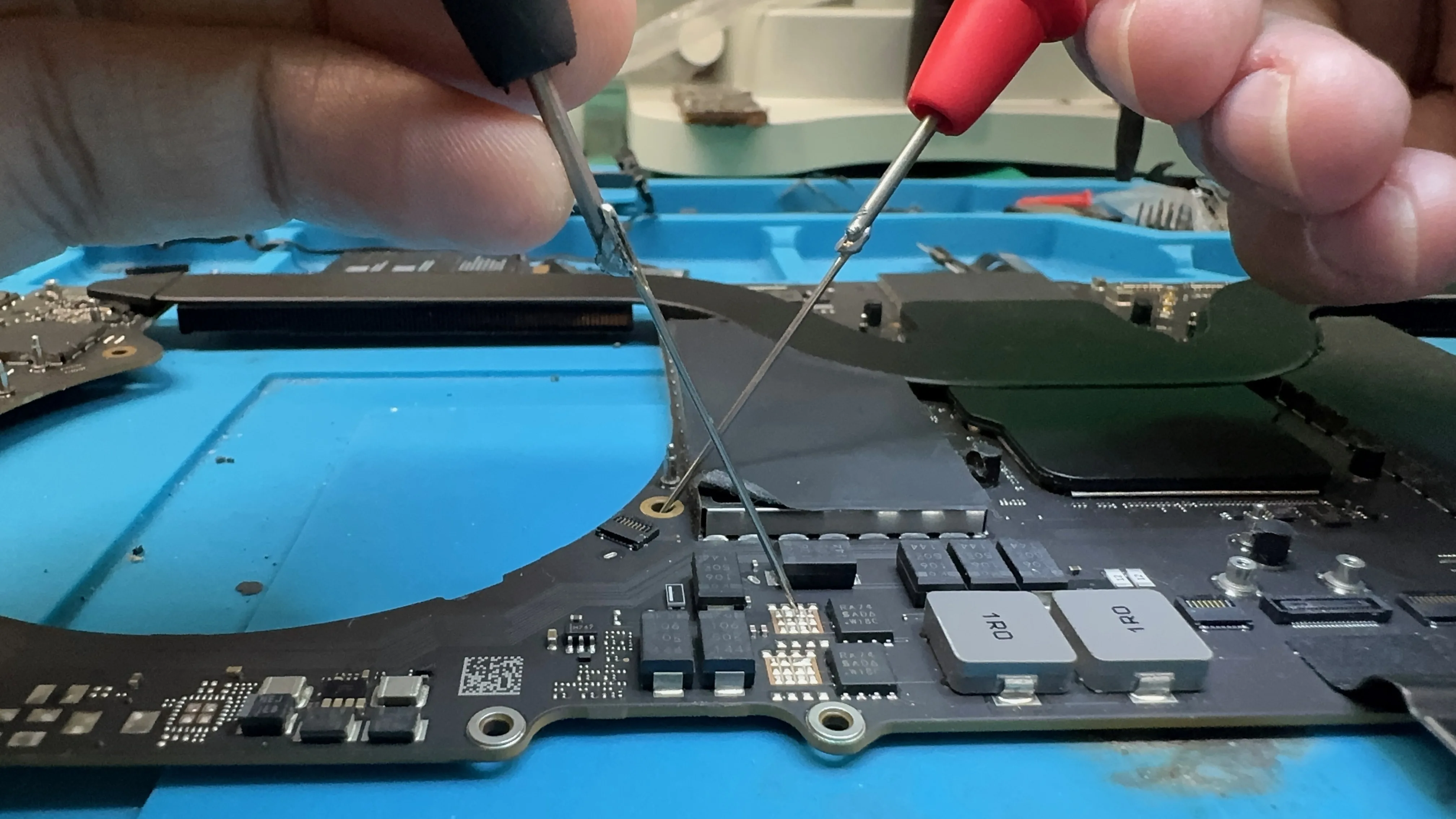 WarriorMac technician probing Mac logic board test points with multimeter at Tampa repair bench