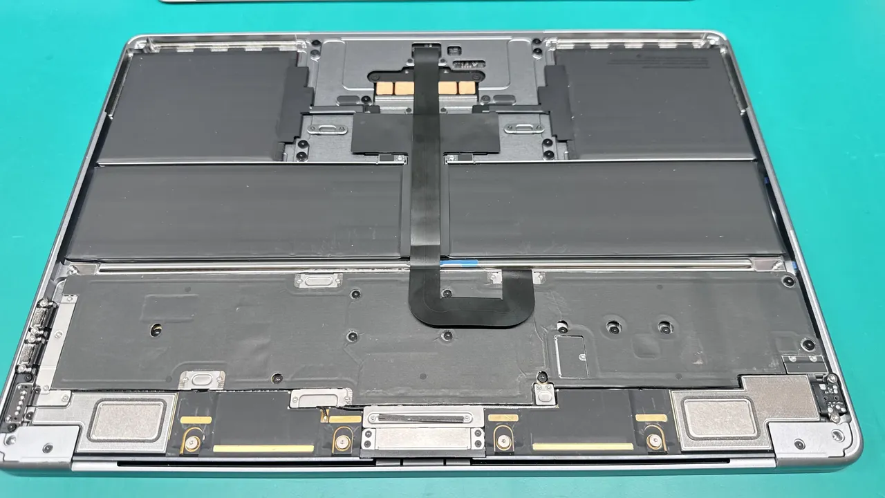 MacBook Air opened showing battery cells and trackpad flex cable during battery replacement service at WarriorMac Tampa