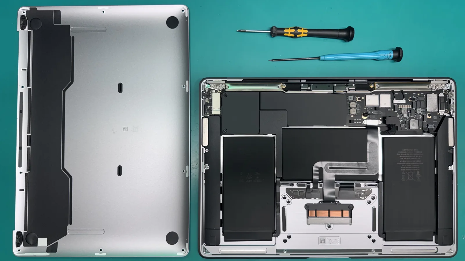 MacBook Air 13-inch M1 2020 opened on the bench with the bottom case removed, showing the logic board, twin battery cells and trackpad before the repair