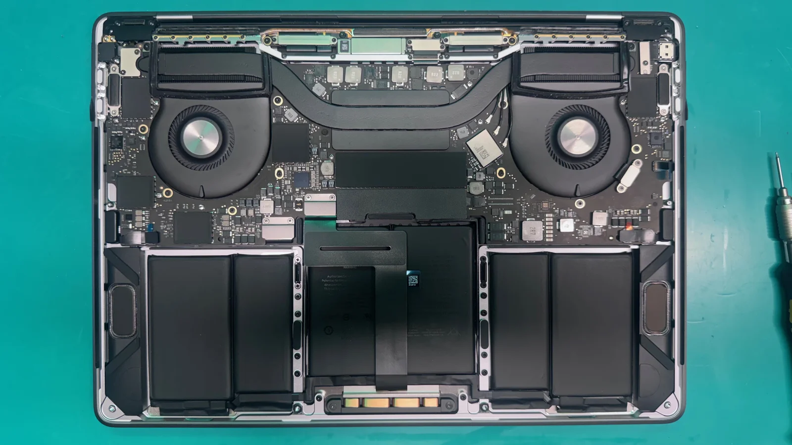 MacBook Pro internals exposed showing battery cells and logic board during repair at WarriorMac Tampa