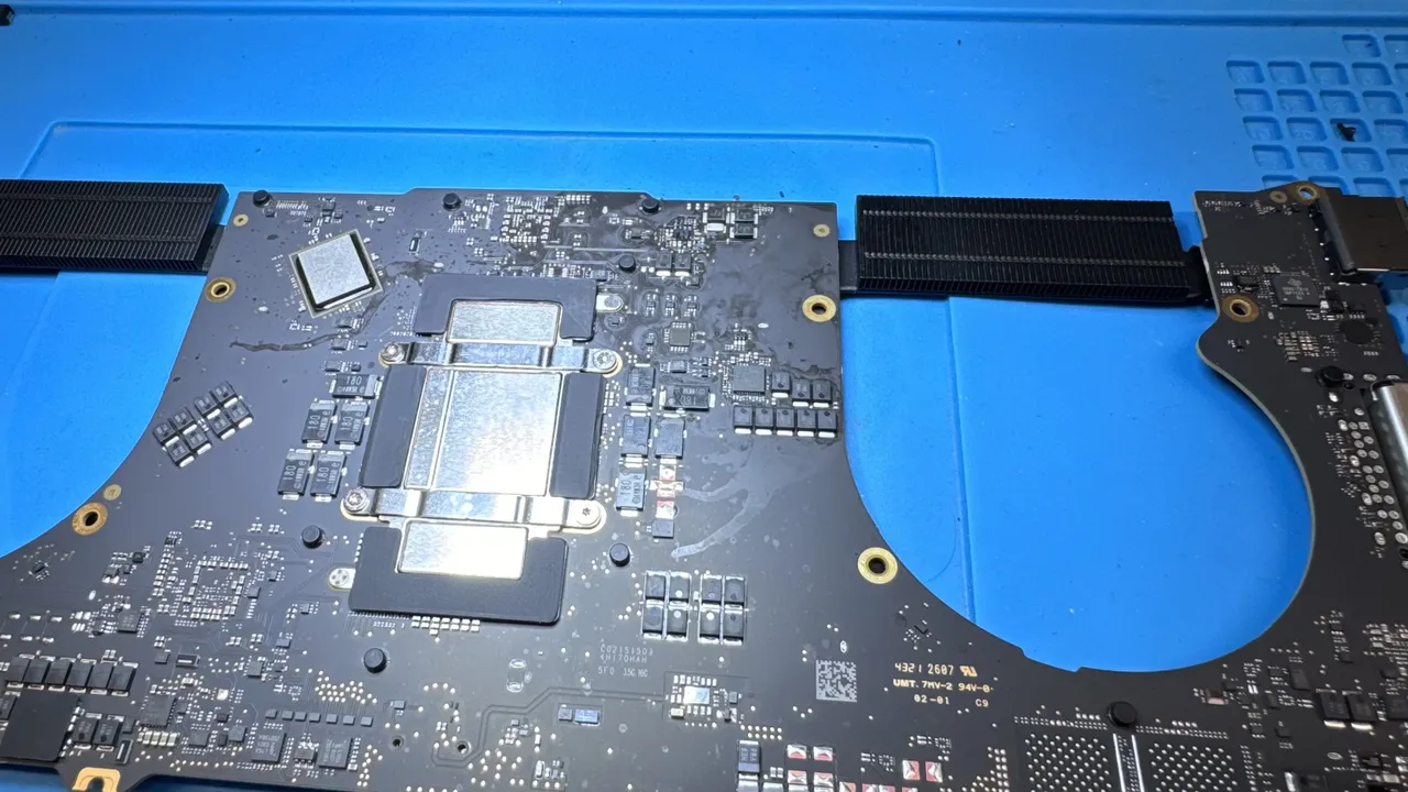 MacBook Pro logic board close-up showing CPU heat spreader, SMD components, and flex cables during component-level repair at WarriorMac Tampa